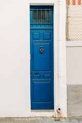 A vibrant blue vintage door stands out against a textured white wall, evoking a sense of history and design.