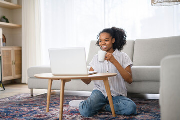 Young woman sitting on floor by the couch using laptop. Afemale working on laptop computer at home.