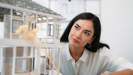 Young beautiful caucasian architect engineer turns house model around to inspect house construction...