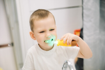 boy brushing teeth in bathroom in front of mirror. oral and dental hygiene. children's toothbrush with backlight