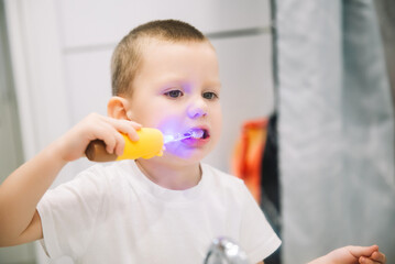 boy brushing teeth in bathroom in front of mirror. oral and dental hygiene. children's toothbrush with backlight