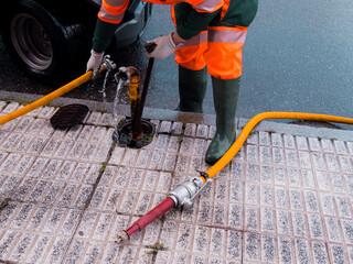 Worker in protective gear using hose for street drainage maintenance