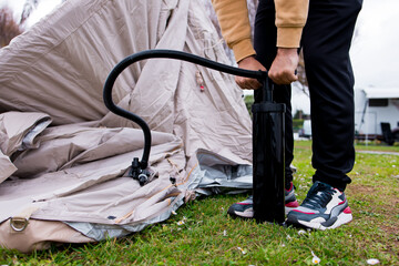 Man inflating tent with hand pump at campsite