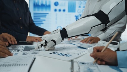A robotic arm assists a business team in analyzing data and creating presentations in a modern office, showcasing the integration of technology and teamwork.Noogenesis