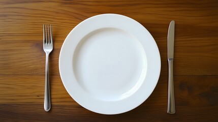White dinner plate with fork and knife on wooden table viewed from above