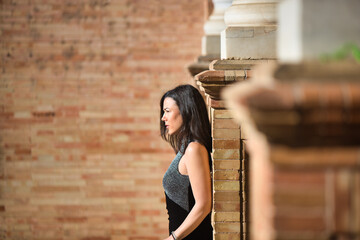 Young and beautiful brunette woman in black dress is in the famous square of spain in sevilla,...