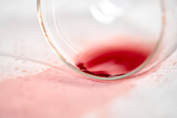 Empty wine glass lies on its side, spilling red liquid onto crisp white tablecloth. Scene captures moment of accidental spill, highlighting stark color contrast and casual atmosphere