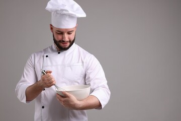 Happy confectioner in uniform holding whisk and bowl on light grey background