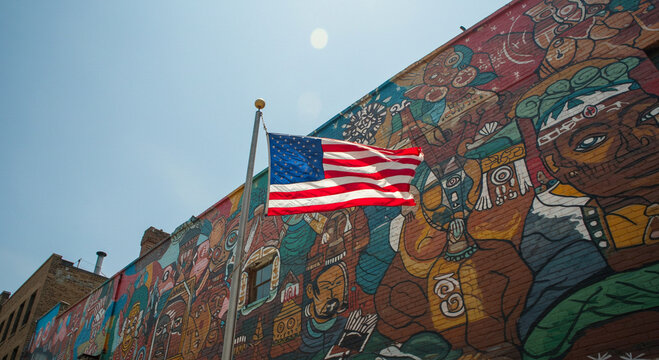 American Flag Flies High Against Vibrant Cultural Mural on Brick Wall