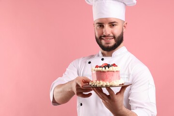 Happy confectioner in uniform holding cake with berries on pink background