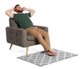 Smiling man in headphones relaxing on armchair and rug against white background