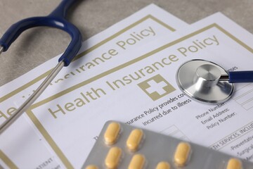 Health insurance policy forms, pills and stethoscope on grey table, closeup