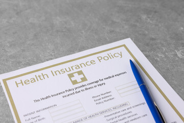 Health insurance policy form and pen on grey table, closeup