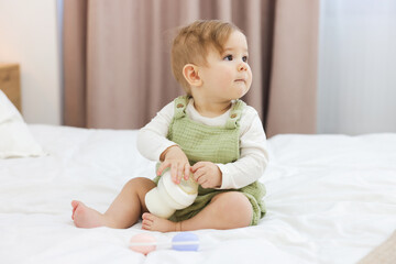 Cute little baby with feeding bottle of milk on bed at home