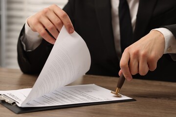 Man stamping licensing agreement document at wooden table indoors, closeup