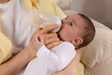 Mother feeding her little baby from bottle indoors, closeup
