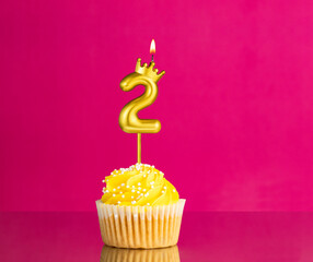 Birthday celebration with number 2 candle - Yellow cupcake on a pink background