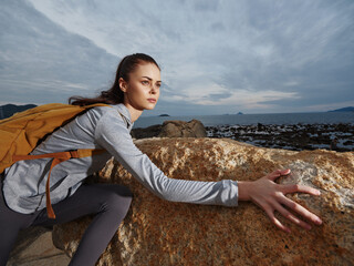 Adventurous young woman climbing rocks near the ocean, showcasing determination and outdoor spirit...