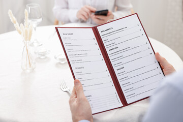 Man with menu at table in restaurant, closeup