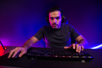 Smart gaming streamer concentrating gaming players trying to pass the level at mission completed, using headset and mic for communicate others on streaming live at neon lighting studio room. Surmise.