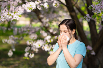 Woman sneezing into tissue in blooming garden, seasonal allergy symptoms during springtime