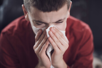 Teen boy sneezing and wiping nose due to cold or allergy