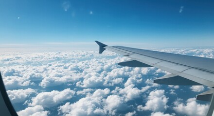Obraz premium View from airplane window showing wing above fluffy white clouds and clear blue sky.