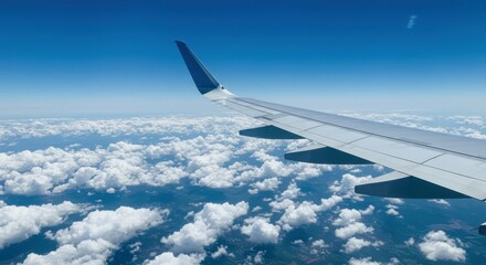 Obraz premium Airplane wing slicing through bright blue sky above soft cloudscape.