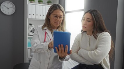 Doctor showing tablet to patient in clinic room, discussing medical information and treatment options with focus on healthcare and professional communication.