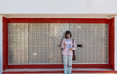 A girl stands near a mailbox on the street and looks through envelopes. A girl with envelopes.