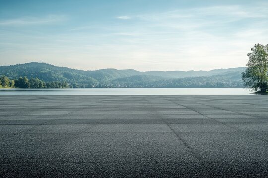 Empty paved area by a serene lake with hills
