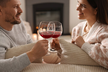 Happy couple clinking glasses of wine on sofa in room with stylish fireplace