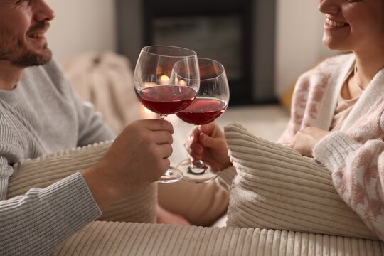 Happy couple clinking glasses of wine on sofa indoors, closeup