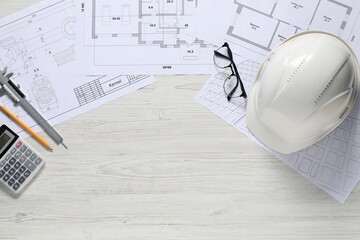 Different architectural drawings, hard hat, pencil, vernier caliper, calculator and glasses on light wooden table, flat lay. Space for text