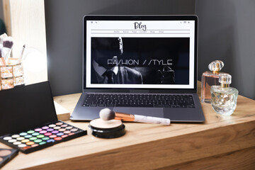 Laptop with fashion blog web site and makeup products on wooden dressing table indoors