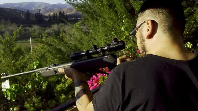 Person Firing a Pellet Air Rifle Viewed from Behind at an Angle on a Hilltop with Scenic Landscape in Coquimbo Region Chile Outdoor Target Shooting Practice