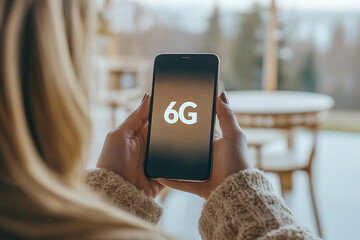 Woman holds a smartphone displaying "6G" technology concept indoors with natural light. Focus on connectivity and future technology trends.