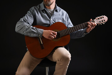 Man playing guitar on chair against black background, closeup