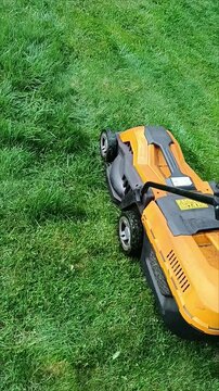 A man mowing green grass in the garden. Gardening at the summer house during the spring and summer seasons. The lawn mowing process taking place outdoors.