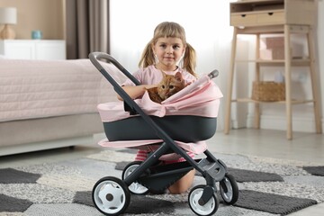 Cute little girl with her ginger cat in doll stroller at home
