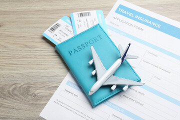 Medical tourism. Travel insurance application form, passport with tickets and airplane model on light wooden background, closeup