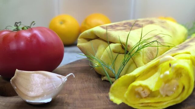 Fresh cheese shawarma lies on a wooden table next to a ripe tomato and a clove of garlic