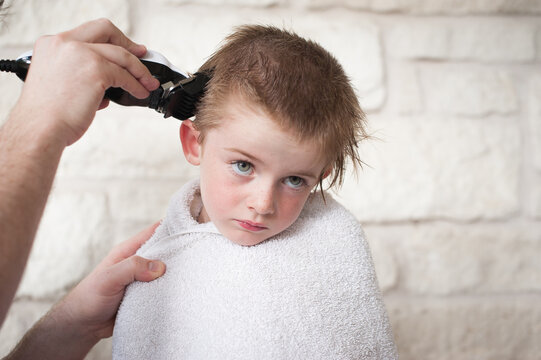 Boy wrapped in a towel getting a buzz hair cut by his father outdoors