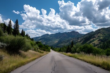 Fototapeta premium A wide asphalt road running through green mountain scenery, with a sunny sky and fluffy white clouds overhead.