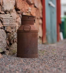 Obraz premium Rusty metal milk can against stone wall.