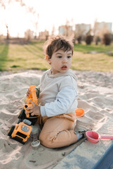 Little boy playing with toy car in the sandbox