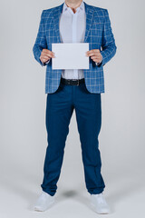 Naklejka premium studio portrait, young elegant stylish man, dressed in blue jacket and trousers, holds white sheet of paper in hands, cropped, unrecognizable, no face, vertical, copy space