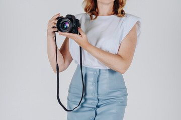 studio portrait, young elegant stylish woman, dressed in blue and white skirt and blouse, holding dslr camera in hands, cropped, unrecognizable, no face