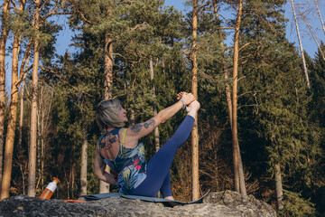 A woman meditating and practicing yoga on top of a rock at sunset, embracing wellness, mindfulness,...
