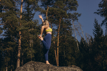 A woman meditating and practicing yoga on top of a rock at sunset, embracing wellness, mindfulness,...